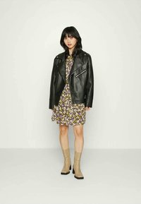 Casaco de biker em couro preto sobre um vestido floral com padrões roxos e brancos; botas de cano curto bege com saltos e solas quadradas pretas.