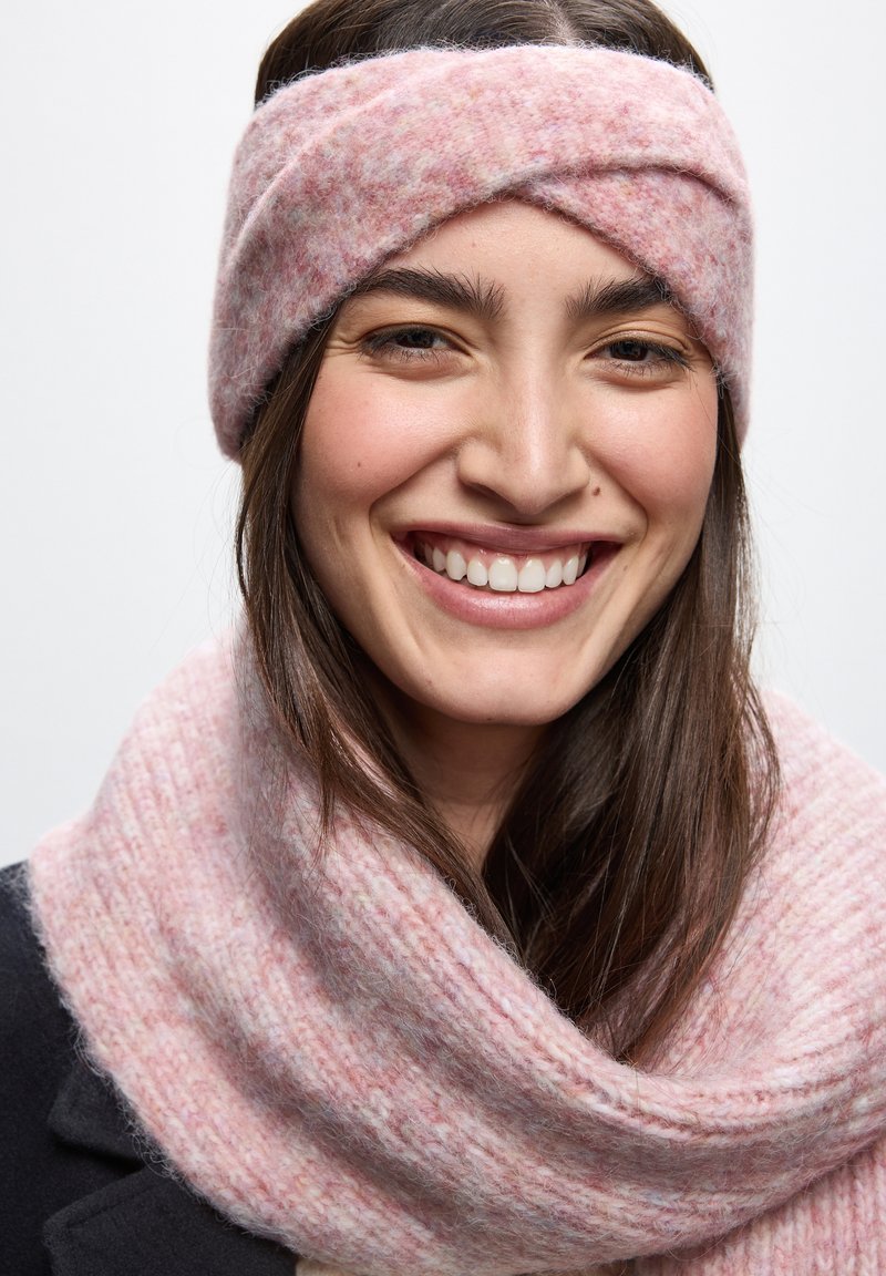 Fascia per la testa lavorata a maglia rosa con un design intrecciato, abbinata a un morbido scaldacollo rosa a coste. Entrambi gli articoli presentano una finitura testurizzata.