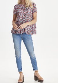 Blouse florale à manches courtes en rouge, bleu et blanc, avec un design peplum ; associée à un jean slim en bleu clair et des sandales à plateforme marron.