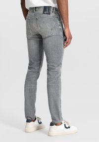 Slim-fit grijze denim jeans met een vervaagde afwerking, voorzien van achterzakken en een leren merkpatch op de tailleband. Gecombineerd met witte sneakers.