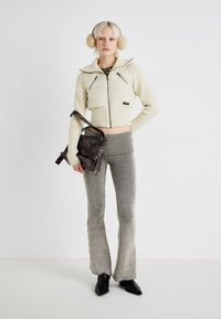 Veste matelassée crème coupée avec ourlet côtelé, haut en maille à carreaux, pantalon en maille gris évasé, et un sac en bandoulière marron foncé. Accessoirisé avec un bandeau pour les oreilles.