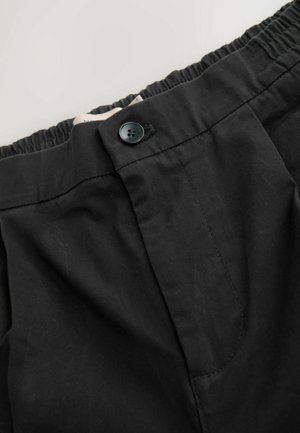 Fekete nadrág rugalmas derékkal és egy gombos záródással. Az anyaga sima, enyhe fényű. Elülső zsebbel rendelkezik.