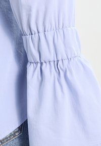 Blusa viola chiaro con maniche arricciate, realizzata in tessuto liscio. Presenta una vestibilità rilassata e una leggera lucentezza, che enfatizza la morbida texture.