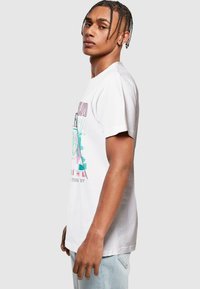 T-shirt en coton blanc à manches courtes avec un imprimé graphique présentant des motifs géométriques colorés et du texte, coupe décontractée, texture lisse.