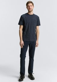 Camiseta de manga corta de un azul oscuro con un patrón, con un bolsillo en el pecho, combinada con pantalones oscuros y botas negras de cordones. Conjunto sencillo y casual.