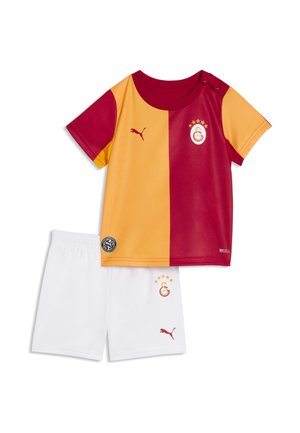 Dziecięcy strój piłkarski Galatasaray z połową żółtej, połową czerwonej koszulki i białymi spodenki, z logo Puma i herbem drużyny.