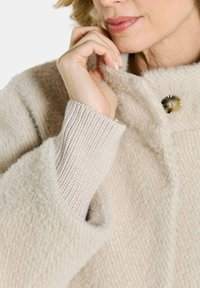 Beige textuur jas met een zachte buitenstof, geribde gebreide mouwen en een ronde knoopsluiting, die een gezellige en casual uitstraling heeft.