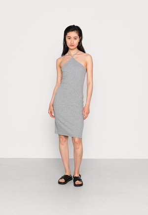 Vestido cinza sem mangas com decote assimétrico, silhueta justa, textura suave, combinado com sandálias pretas planas.