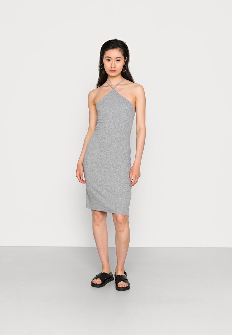 Vestido cinza sem mangas com decote assimétrico, silhueta justa, textura suave, combinado com sandálias pretas planas.