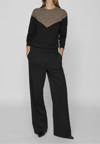 Pantaloni neri e un maglione a blocchi di colore nero e marrone con un design a zigzag. Il maglione presenta un collo rotondo e polsini a coste.