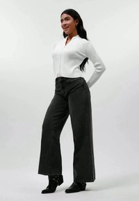 Hvit ribbestrikket cardigan, høytlivde svarte vide jeans og svarte ankelstøvler. Enkel design med avslappet passform og ingen synlige mønstre.
