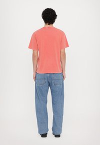 Rdzaworudy t-shirt z krótkim rękawem o luźnym kroju, połączony z jasnoniebieskimi spodniami typu wide-leg z dwiema tylnymi kieszeniami.