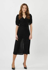 Abito midi nero con maniche a palloncino corte, busto arricciato e spacco anteriore. Tessuto liscio con leggero lucido. Indossato con decolleté neri a punta.