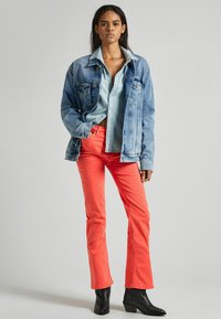 Denimová bunda s svetlom modrou košeľou a koralovými rozšírenými nohavicami. Čierne členkové topánky dotvárajú outfit. Hladká tkanina a prispôsobený strih.