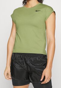 Camiseta atlética de manga corta en verde oliva con rayas y un logotipo negro de Nike, combinada con pantalones cortos de gimnasio brillantes negros.