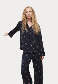 Marineblauw pyjamaset met een overhemd met knopen en lange mouwen en een broek met elastische taille, beide versierd met kleurrijke harten en kersen.