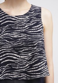 Top senza maniche blu navy con un motivo a strisce bianche ondulate, realizzato in tessuto leggero con una consistenza morbida e scollo rotondo.