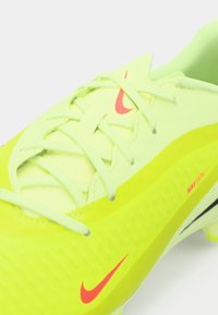 Lys gul fodboldstøvle med struktureret overflade, spidset form og pink Nike-logo. Har matchende snørebånd og et strømlinet design.