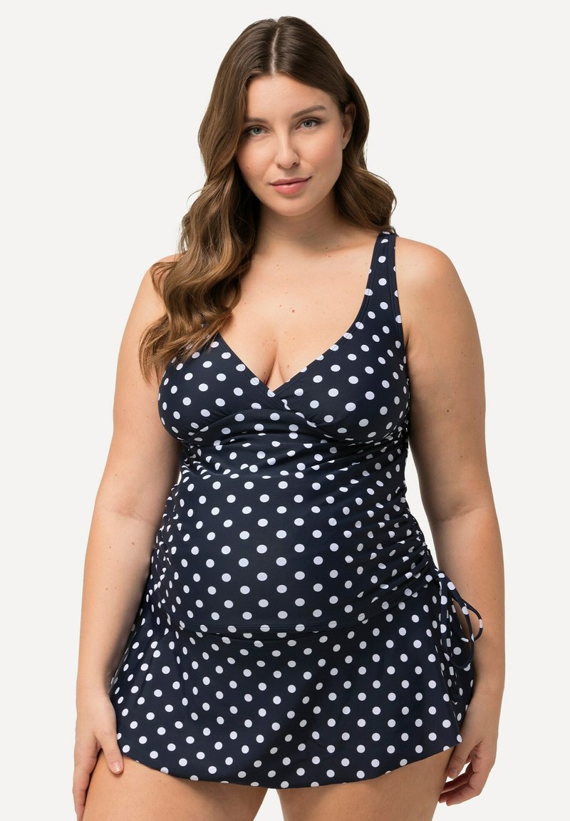 Robe de bain à pois bleu marine avec liens latéraux réglables, détails en tissu froncé et décolleté en V. Fabriquée en tissu extensible pour un confort optimal.