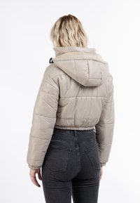 Avkortad pufferjacka i ljus beige med huva, med sydda sektioner och elastiska manschetter. Matchad med högmidjade svarta jeans.