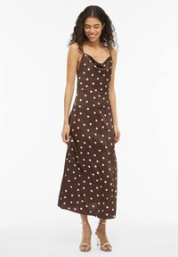 Rjava satenasta obleka z ovratnikom v obliki kapuce, tankimi naramnicami in belimi pikami, ki ima tekočo silhueto in dolžino do sredine meč. Dopomorejo ji sandali z naramnico.