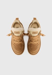 Pantofi din suede maro și textil, cu căptușeală pufoasă, având șireturi legate în noduri și un logo cusut. Designul superior este texturat și structurat.