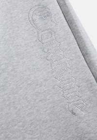 Pelēkā sporta jaka ar strukturētu dizainu, kurā ir rhinestones, kas vertikāli uzrakstīti "Couture" gar audumu. Mīksts kokvilnas maisījuma materiāls.