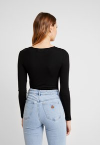 Must have pikkade varrukatega must pluus, mis on kombineeritud helesiniste kõrge vöökohaga teksadega, mille tagakotil on kolmnurkne plaaster. Sile tekstuur, minimalistlik disain.