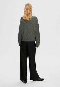 Grauer Wollpullover mit einem verkürzten Design, lockeren Ärmeln und geripptem Saum, kombiniert mit weiten schwarzen Hosen und flachen schwarzen Schuhen.