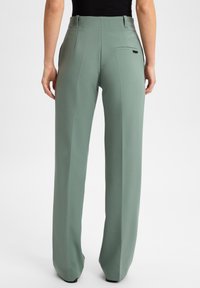 Groene, hoge taille, ruime broek gemaakt van soepel materiaal. Voorzien van een achterzak en een vouw aan de voorkant. Minimalistisch ontwerp.