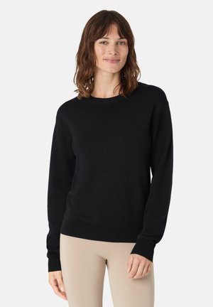 Pull en maille noir avec manches longues, encolure ronde, et poignets et ourlet côtelés. Texture lisse avec une silhouette ajustée.