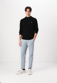 Maglione nero a coste con logo giallo, abbinato a pantaloni azzurri chiari e sneakers bianche. Design semplice in una palette di colori neutri.
