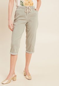 Pantalons cropped vert clair avec une taille à cordon, des poignets retroussés et une texture lisse. Portés avec des chaussures à talons carrés dorés.