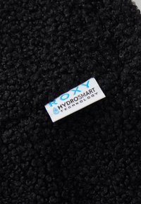 Tela negra texturada con un acabado de bucle, que presenta una etiqueta blanca que dice "ROXY HYDROSMART TECHNOLOGY" en letras azules.