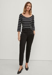 Zwarte broeken met een slim fit en zijritsen, gecombineerd met een marineblauw gestreept langslijf t-shirt. Materiaal lijkt zacht en textuur te hebben. Zwarte slingback schoenen.