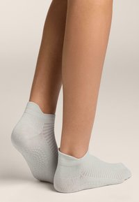 Világosszürke boka zokni, texturált kötött anyagból, bordás szegéllyel és erősített sarokkal, csúszásmentes tapadási mintával.