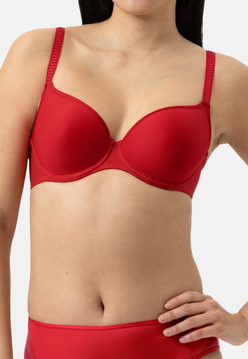 Punainen pehmustettu rintaliivi, jossa on säädettävät hihnat, sileä rakenne, tuki langalla ja saumaamaton muotoilu. Esitelty yhdessä vastaavien punaisten alushousujen kanssa.