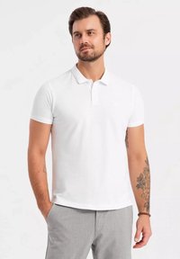 Valkoinen lyhythihainen polo paita, jossa on kaulus, teksturoitu kangas ja slim fit -leikkaus. Yhdistetty vaaleanharmaisiin housuihin, joissa on hienovarainen logotieto.