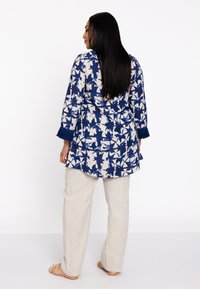 Blauw en crèmekleurige tuniek met een patroon en franjes aan de mouwen, gecombineerd met lichtbeige linnen broeken met een relaxte pasvorm en zachte textuur.