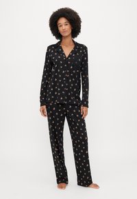 Set de pijama negru cu un model floral, mâneci lungi, cămașă cu nasturi și buzunar, și pantaloni largi asortați. Textură de țesătură netedă.