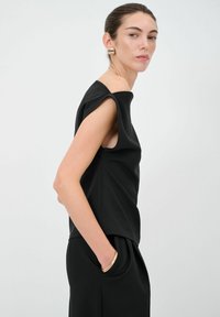 Top nero senza maniche con design strutturato e spalle larghe, abbinato a pantaloni neri sartoriali. Tessuto testurizzato con uno stile minimalista.