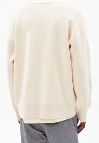 Maglione oversized beige chiaro con orlo e polsini a coste, caratterizzato da un tessuto testurizzato e una vestibilità rilassata. Mostrato in vista posteriore.