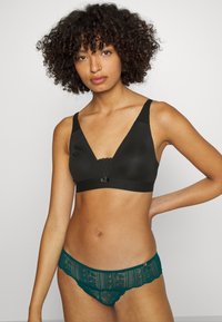 Czarny, teksturowany biustonosz z dekoltem w kształcie V, koronkowym wykończeniem i regulowanymi ramiączkami. Turkusowe majtki koronkowe z finezyjnymi wzorami i falbaniastymi brzegami.
