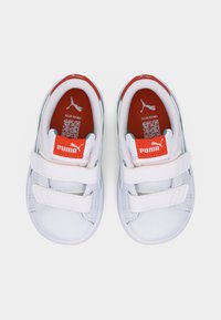 Λευκά παπούτσια Puma για νήπια με διπλά λουράκια Velcro, πορτοκαλί εσωτερικές σόλες με λογότυπο Puma και κωδικούς QR.