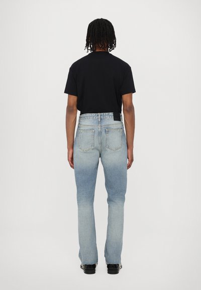Tricou negru cu mânecă scurtă asociat cu blugi de denim de culoare albastru deschis. Blugii au un finisaj ușor uzat și margini desfăcute.