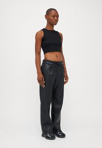 Zwarte cropped tanktop en hooggewaiste zwarte leren broek, met een trekkoord in de taille en een gladde textuur, gecombineerd met zwarte sneakers.