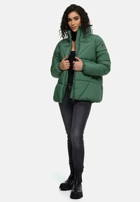 Groene pufferjas met een hoge kraag, textuurstof en gewatteerd ontwerp. Beschikt over zijzakken en een rits aan de voorkant.