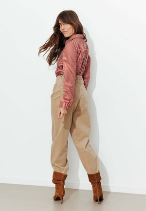 Chemise à rayures rouges et blanches à boutons avec manches longues, associée à un pantalon en velours côtelé beige taille haute et des bottines marron.