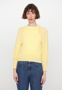 Hellgelber Pullover mit geripptem Saum und Bündchen, mit Rundhalsausschnitt und langen Ärmeln, kombiniert mit blauen Jeans.