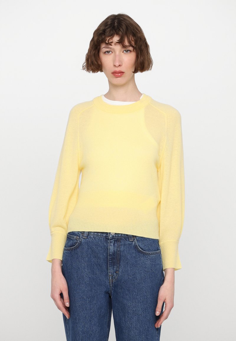 Hellgelber Pullover mit geripptem Saum und Bündchen, mit Rundhalsausschnitt und langen Ärmeln, kombiniert mit blauen Jeans.